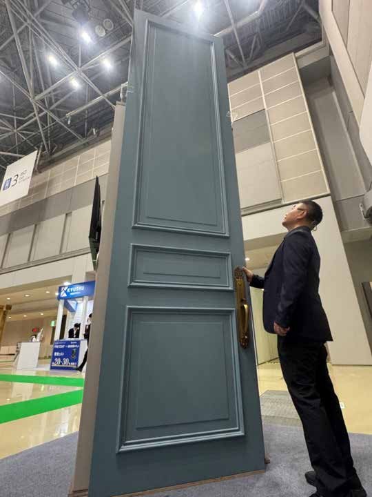 第32屆日本東京建築・建材展中參觀者仰望 4 米深色超高門片