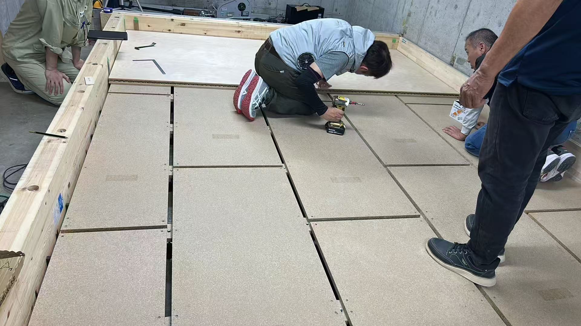 日本技師跪地以電動起子固定乾式架高隔音地板板材並進行水平調校